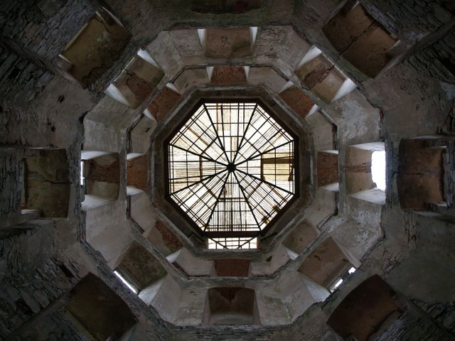 This striking view of a weathered octagonal dome interior with rustic window grills can add an element of historic beauty to architectural portfolios, educational exhibits on ancient structures, or as a unique visual piece in creative art installations.