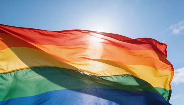 Backlit rainbow pride flag waving in sunlight against blue sky