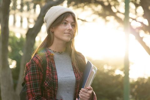 Student Wearing Beanie and Plaid Shirt Walking at Golden Hour Holding Notebooks