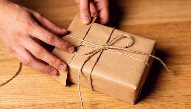 Hands wrapping rustic gift with kraft paper and jute twine on wooden table