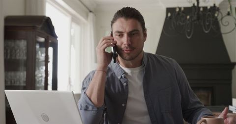 Man Multitasking with Smartphone and Laptop in Home Office