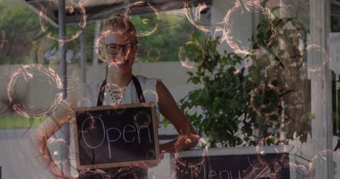 Smiling Woman Holding Open Sign at Outdoor Cafe Welcoming Customers with Cheerful Energy