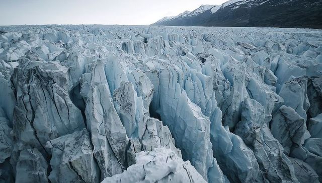 Jagged glacier ice field stretching across alpine valley with deep crevasses and seracs