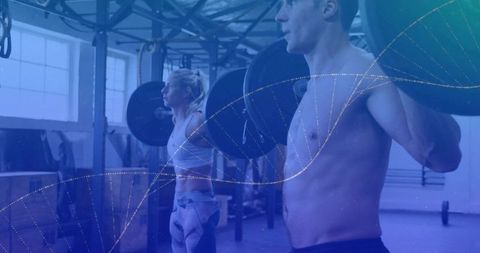 Shirtless man and woman lifting barbells together at industrial gym for strength training