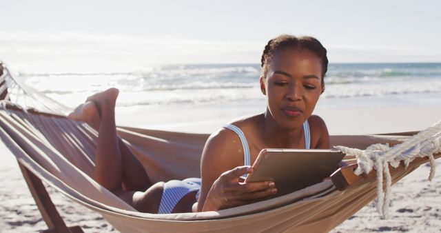 African american woman using digital tablet while lying on a hammock at the beach. travel vacation lifestyle concept