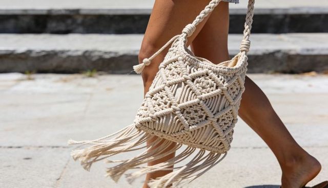 Walking barefoot on sunlit pavement with boho macrame fringe bag swinging summer style