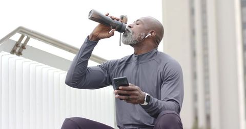 Senior African American Man Hydrating After Urban Workout Wearing Earbuds and Smartwatch