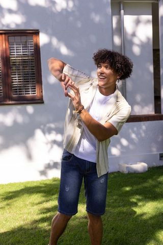 Smiling young man enjoying sunlit backyard with dappled tree shadows and casual summer