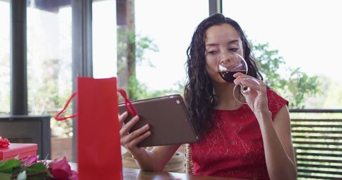 Woman in Red Dress Enjoying Wine While Video Calling on Tablet