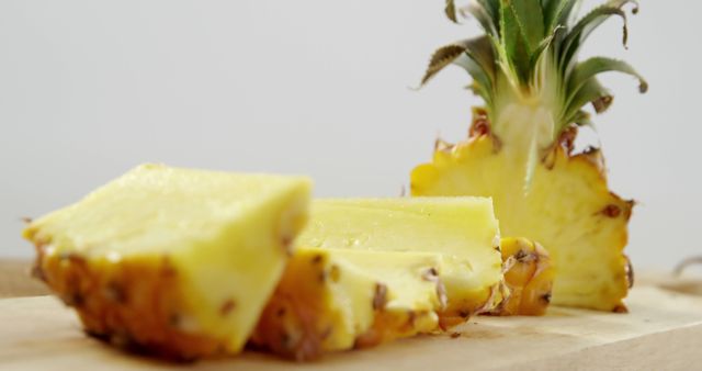 Fresh pineapple slices on a wooden cutting board present a delicious and healthy snack option. The vibrant yellow fruit, known for its tropical sweetness, is perfect for culinary usage in desserts, salads, smoothies, or as a standalone treat. Ideal for promoting healthy eating, organic foods, and summer recipes.