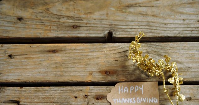 Happy thanksgiving text on brown tag and gold decoration with copy space lying on wooden planks. Thanksgiving, celebration and writing, unaltered.