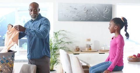 African american father folding laundry with daughter sitting on counter smiling together
