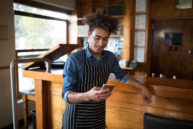 Smiling waiter using mobile phone at counter in bar