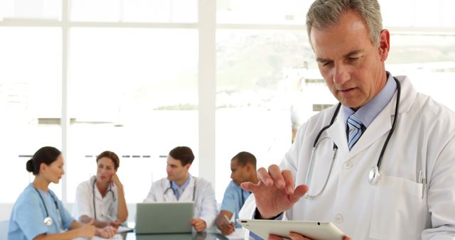 Male Doctor Using Digital Tablet with Medical Team Meeting in Background - Download Free Stock Images Pikwizard.com