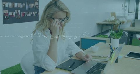Blonde professional talking on phone while working on laptop in bright coworking office