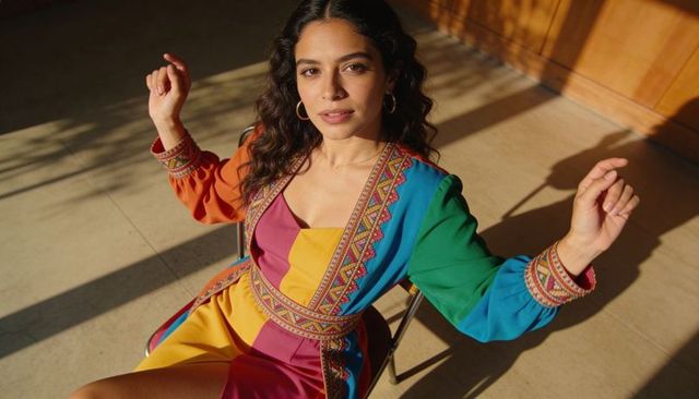 Sitting woman wearing colorful embroidered patchwork dress casting sunlit shadows