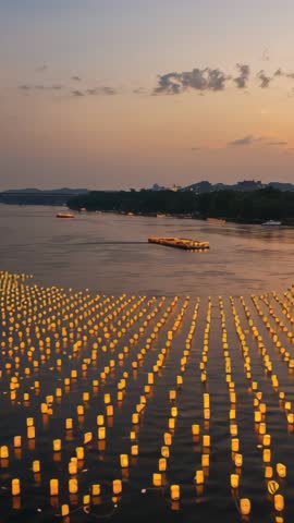Vertical video capturing drifting lanterns glowing on river at dusk with barge restocking