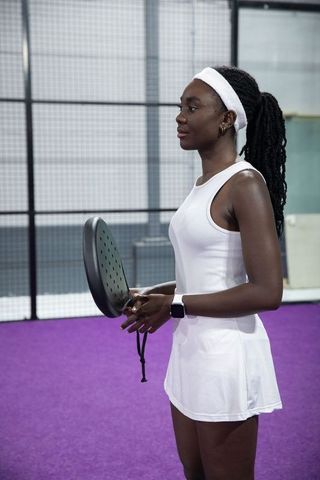 African american woman preparing for padel match on indoor purple court in white sportswear