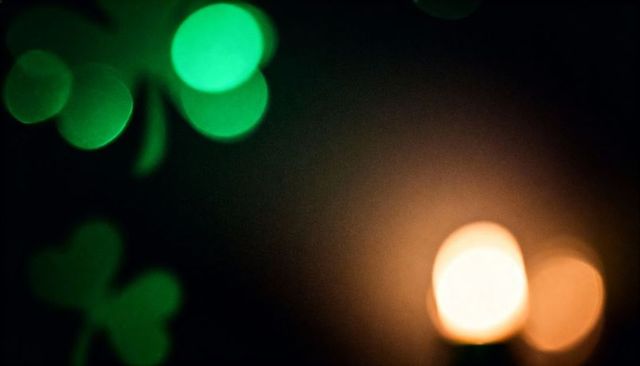 St patrick bokeh with amber candlelight and green clover silhouettes on dark background