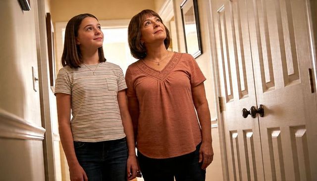 Mother and teen daughter standing in hallway looking up showing warm family bond
