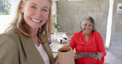 Women in professional attire smile while working together, showcasing a collaborative office atmosphere. Great for illustrating positive workplace cultures, diversity in business, or technological interaction among professional women.