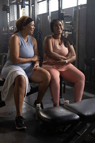 African american women laughing and resting on weight bench after workout in gym