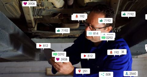 Mechanic under vehicle engaged with digital technology