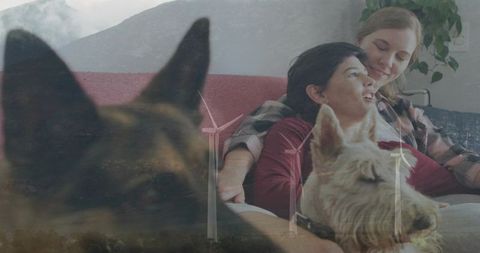 Couple cuddling with dogs on couch with wind turbine landscape double exposure