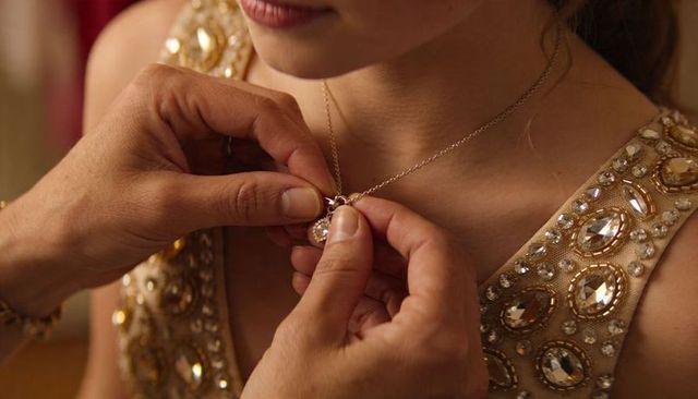 Fastening pendant necklace on bride wearing gold embellished gown, close-up detail