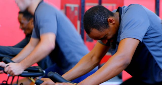 Individuals riding stationary bikes in gym. Can be used for promoting fitness classes, gym memberships, healthy lifestyle, motivational content, or workout routines.