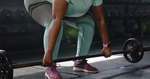 African american woman performing barbell deadlift in gym wearing mint leggings, strength