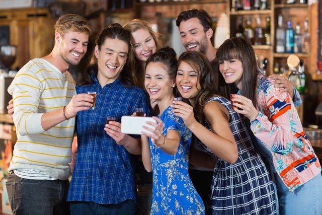 Group of friends taking a selfie while holding drinks in a bar. They are smiling and appear to be having a good time. This image can be used for promoting social events, nightlife, friendship, and celebration themes.