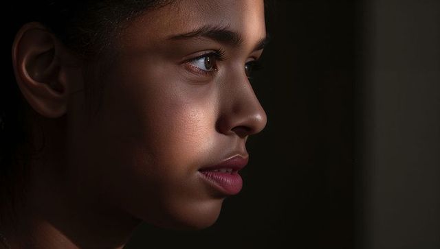 Gazing teenage girl profile in low-key lighting highlighting skin texture and emotion