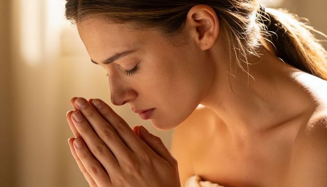 Young woman praying in warm sunlight, contemplative closeup portrait for wellness