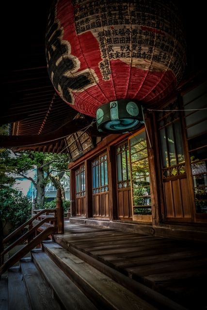 The image depicts the entrance of a traditional Japanese temple, featuring a large red paper lantern with black and white characters above the wooden stairs. This serene and culturally rich setting is perfect for use in content focused on Japanese culture, travel destinations, spiritual retreats, or architectural beauty. It can also complement editorials about Asian sacred places or serene environments.