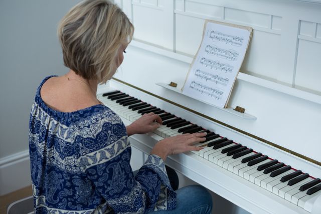 A woman is practicing piano at home, concentrating on sheet music in a casual setting. Can be used for themes of learning, music education, creativity, hobbies, and relaxation.