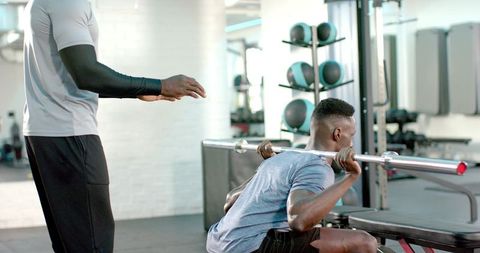 Trainer Spotting African American Athlete Performing Barbell Back Squat in Commercial Gym