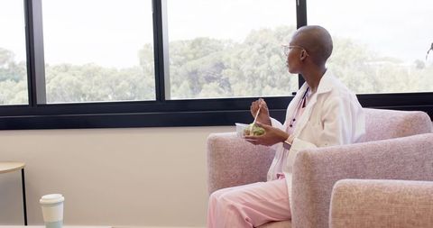 African american healthcare professional taking lunch break by window holding salad
