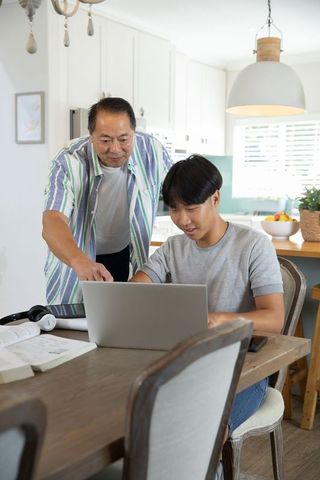Asian Father and Son Engaged in Collaborative Learning at Kitchen Table