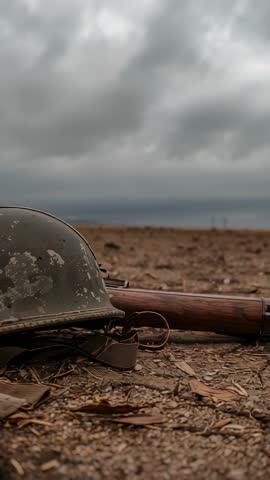 Gusty wind tossing leaves around chipped military helmet and rifle on barren plain | Vertical video