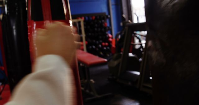 Hand punching red punching bag in gym with blurred motion conveying dynamic action. Ideal for use in content related to fitness, sports training, boxing, martial arts, and physical exercise routines.