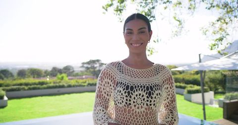 Smiling woman standing on sunlit terrace wearing white crochet top and black bikini