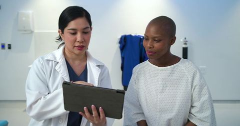 Clinician reviewing tablet with patient in gown during compassionate hospital consultation