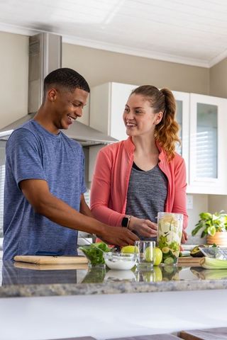 Couple preparing healthy green smoothie at kitchen island, smiling and chatting