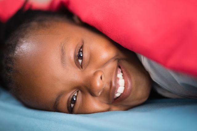 This image captures a close-up of a smiling girl lying on a bed, conveying a sense of happiness and comfort. Ideal for use in advertisements, blogs, or articles related to childhood, family life, home comfort, and well-being.