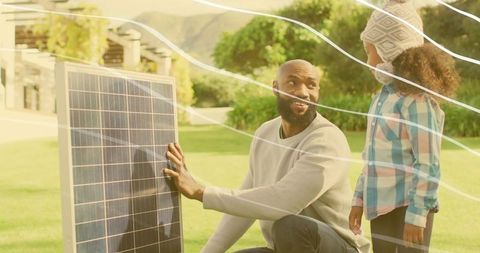 Father teaching daughter about solar panel while kneeling in sunny suburban backyard