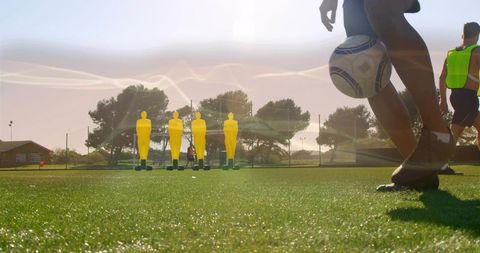Player kicking ball past training dummies on sunny football turf