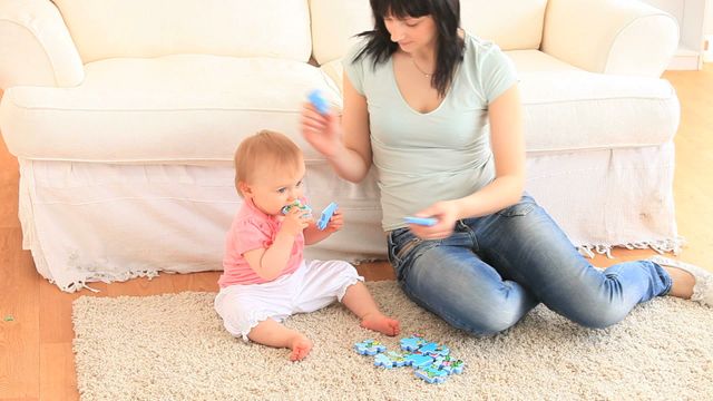 Mother and daughter are sitting on the carpet in the living room playing with puzzle pieces. The interaction captures family bonding and the early learning process through play. It can be used to depict themes of parenting, childhood development, home activities, and family leisure.