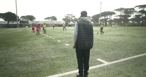 Coach Observing Soccer Players During Training on Sunny Field