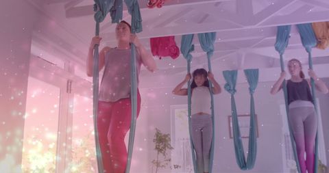Instructor and teens practice aerial yoga amidst glowing particles